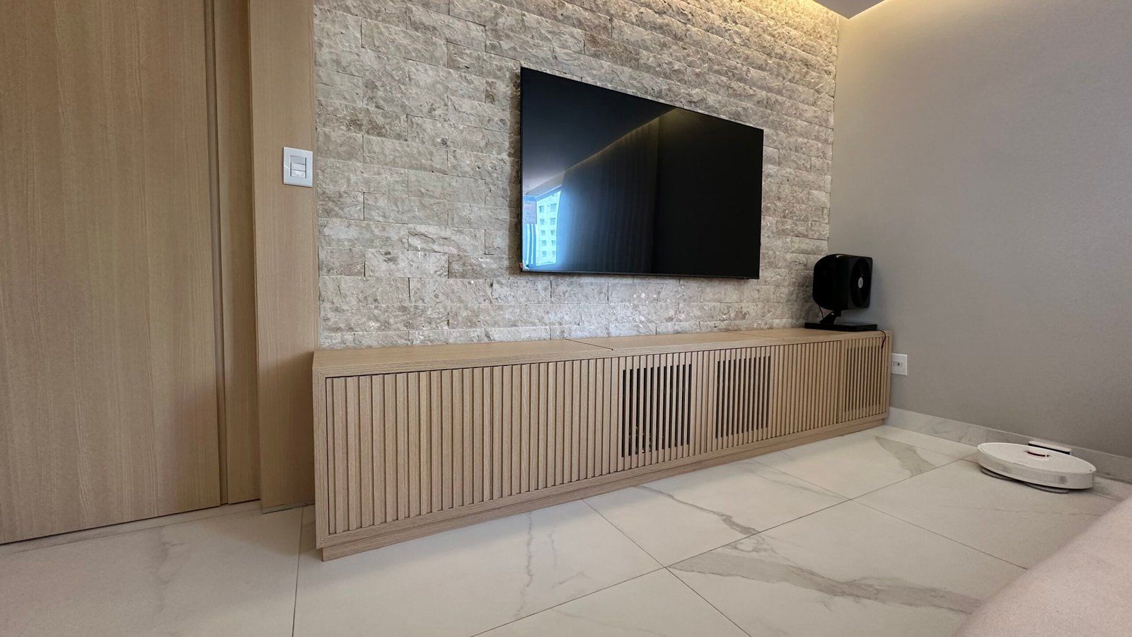 Painel de TV ripado em madeira clara sobre parede de pedra